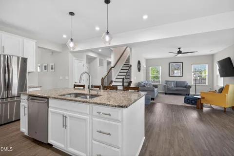 a kitchen with stainless steel appliances granite countertop a refrigerator a sink dishwasher a dining table and chairs with wooden floor