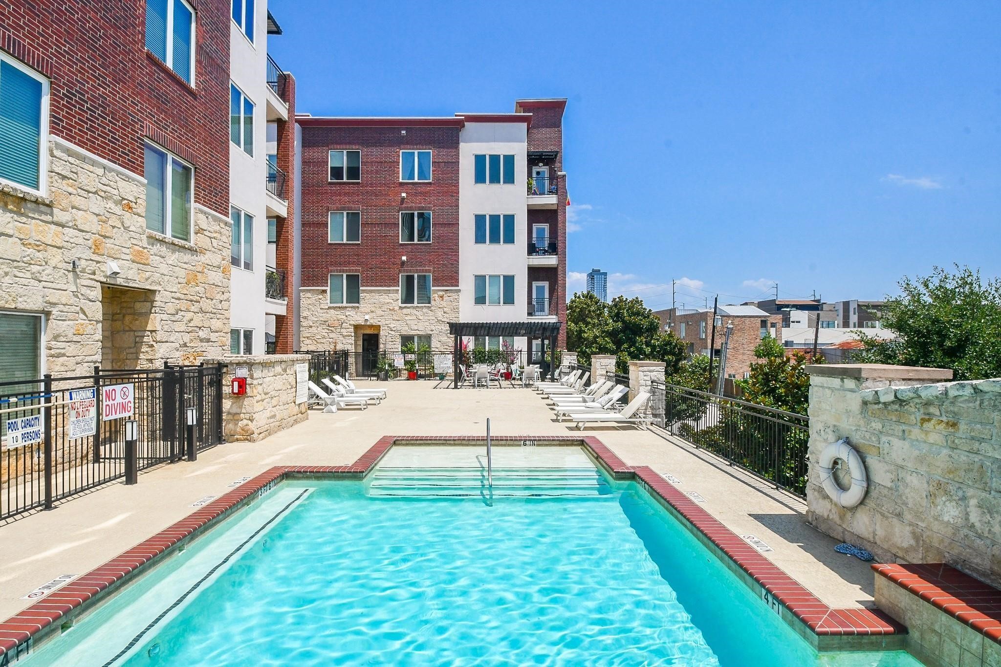 1900 Genesee Street, Unit 203 Houston, TX 77006 - Photo 26 of 30 This photo showcases a modern complex with a refreshing outdoor pool, surrounded by a spacious sun deck and lounge chairs. The building features a combination of stone and brick exterior, offering a stylish and inviting atmosphere.