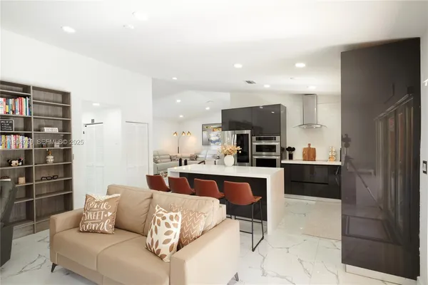 a living room with stainless steel appliances kitchen island granite countertop a refrigerator and a stove top oven