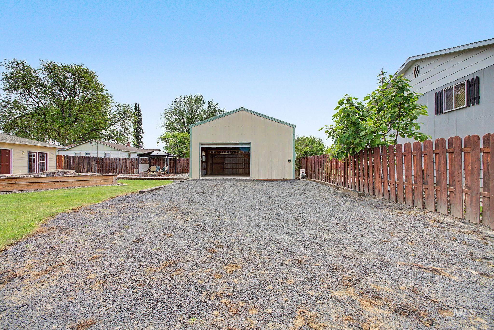 3314 6th Street Lewiston, ID 83501 - Photo 41 of 50 Detached garage with an open bay and gravel driveway, featuring a wood fence, grassy area, and mature trees