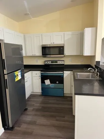 a kitchen with stainless steel appliances a stove a sink a refrigerator white cabinets and a microwave