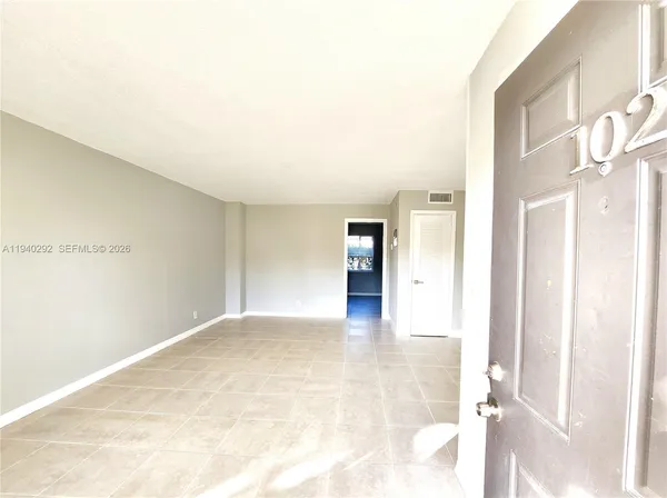 a view of an empty room with kitchen and a window