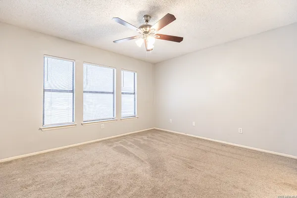 an empty room with chandelier fan and windows