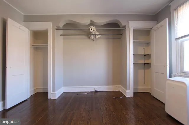 an empty room with wooden floor closet and windows