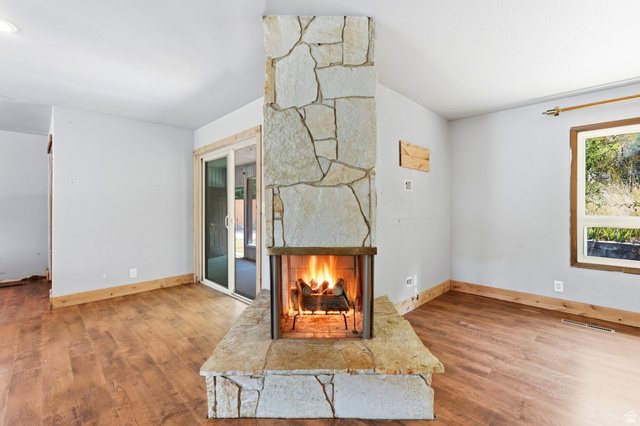 1410 Sumac Drive Logan, UT 84321 - Photo 9 of 28 Central stone fireplace with hearth, wood-finish flooring, white walls, and a sliding glass door