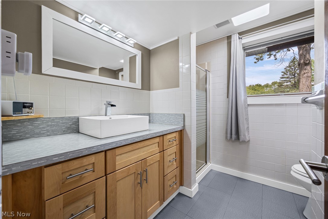 17583 Shurmer Road Strongsville, OH 44136 - Photo 25 of 50 Bathroom featuring a modern vessel sink with a chrome faucet, a wood-finish vanity with ample storage, a framed rectangular mirror, and a tiled shower enclosure