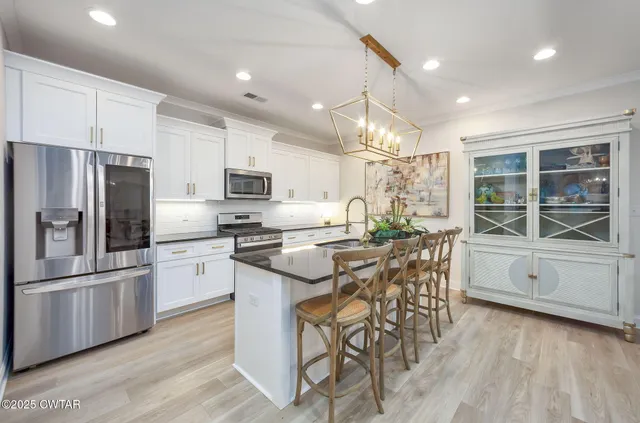 a kitchen with stainless steel appliances granite countertop a refrigerator a stove a sink a dining table and chairs with wooden floor