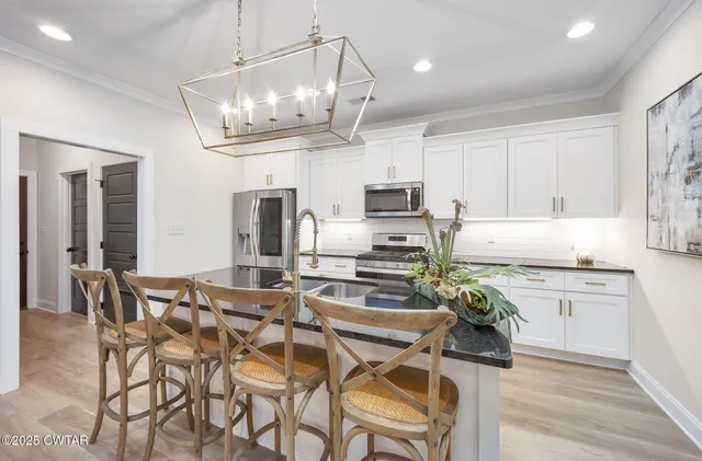 a kitchen with stainless steel appliances granite countertop a stove top oven a refrigerator a sink and chairs