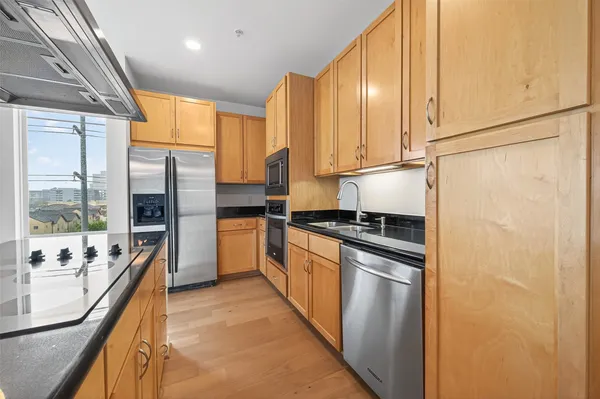 a kitchen with stainless steel appliances granite countertop a refrigerator a sink dishwasher a stove and white countertops with wooden floor