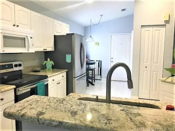 a kitchen with stainless steel appliances kitchen island granite countertop a refrigerator a stove top oven and sink with wooden floor