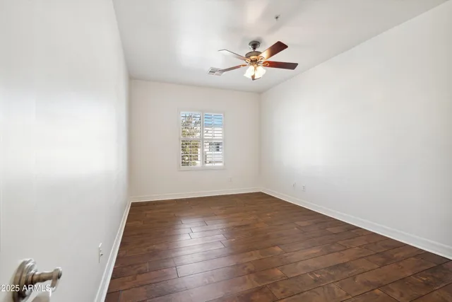 an empty room with wooden floor chandelier fan and windows