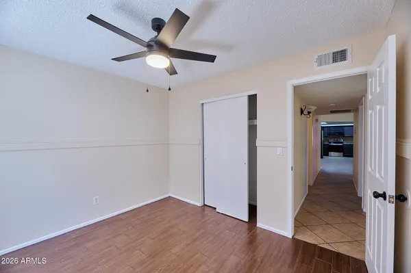 an empty room to hallway with wooden floor a ceiling fan and a kitchen