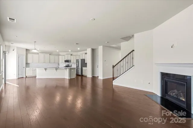 a view of an empty room with wooden floor and a kitchen