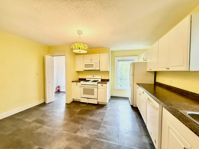 a large kitchen with stainless steel appliances a stove a sink and white cabinets with wooden floor