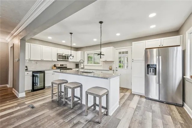 a kitchen with stainless steel appliances granite countertop a refrigerator a sink dishwasher a stove and white cabinets with wooden floor