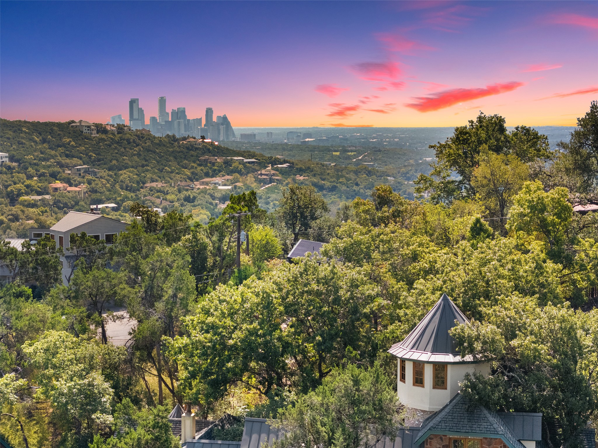 1354 The High Road Austin, TX 78746 - Photo 4 of 40 A striking city skyline emerges over a verdant landscape under a colorful evening sky.
