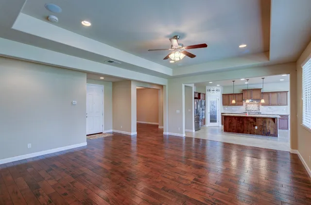an empty room with wooden floor fireplace and a kitchen view