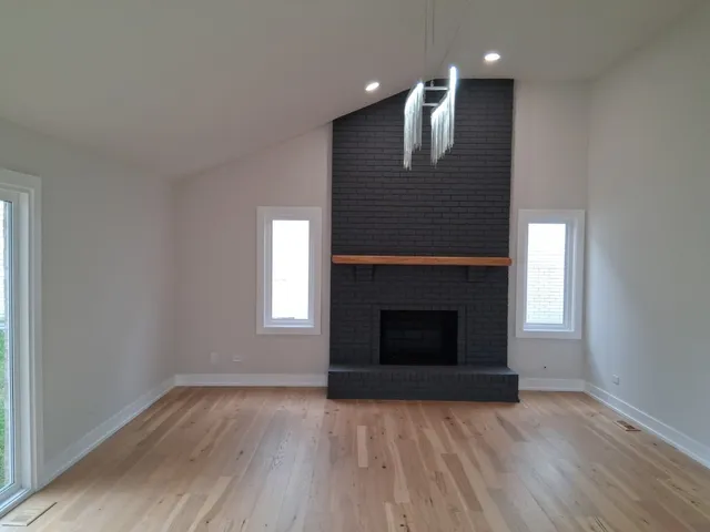 an empty room with wooden floor fireplace and windows