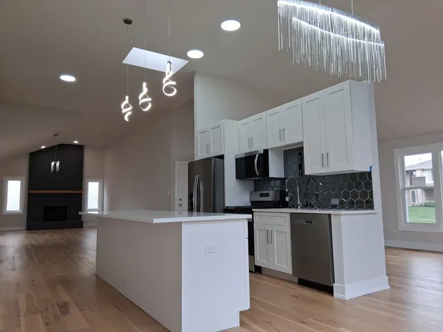 a kitchen with stainless steel appliances kitchen island granite countertop a refrigerator a sink dishwasher and a stove with wooden floor