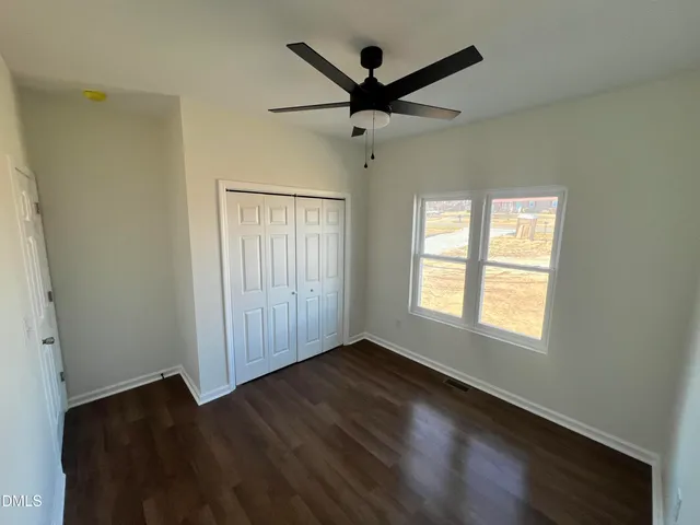 an empty room with wooden floor fan and windows