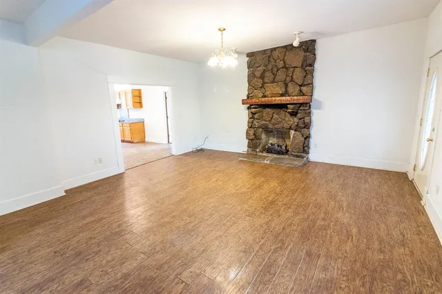 an empty room with wooden floor fireplace and windows