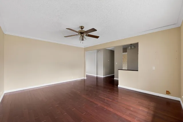 a view of an empty room with wooden floor and a ceiling fan