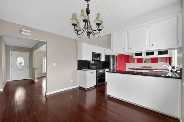 a kitchen with stainless steel appliances granite countertop a refrigerator a stove top oven a sink dishwasher and white cabinets with wooden floor