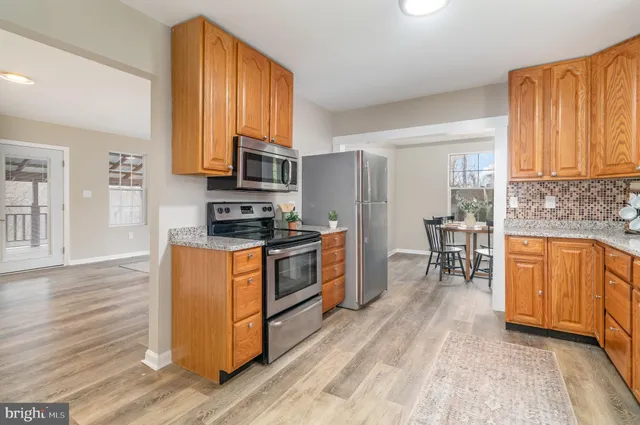 a kitchen with stainless steel appliances granite countertop wooden cabinets a sink dishwasher a stove and a refrigerator with wooden floor