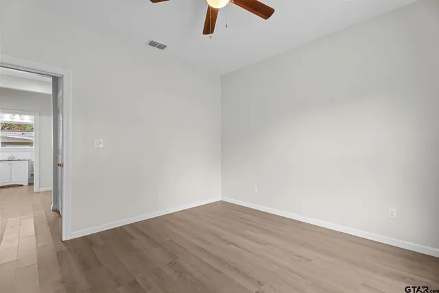 a view of an empty room with wooden floor and a ceiling fan
