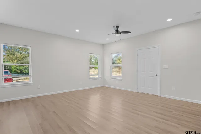 an empty room with wooden floor chandelier fan and windows