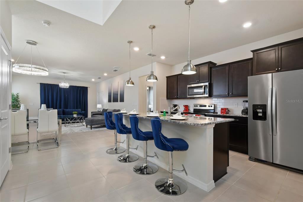 4428 Kaipo Road Davenport, FL 33897 - Photo 5 of 73 a kitchen with stainless steel appliances kitchen island granite countertop a refrigerator a stove a sink with a dining table and chairs