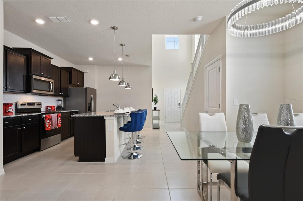4428 Kaipo Road Davenport, FL 33897 - Photo 9 of 73 a kitchen with stainless steel appliances kitchen island granite countertop a refrigerator a stove a microwave oven a sink with island and chairs