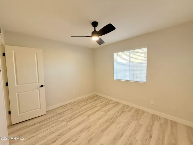 an empty room with wooden floor ceiling fan and windows