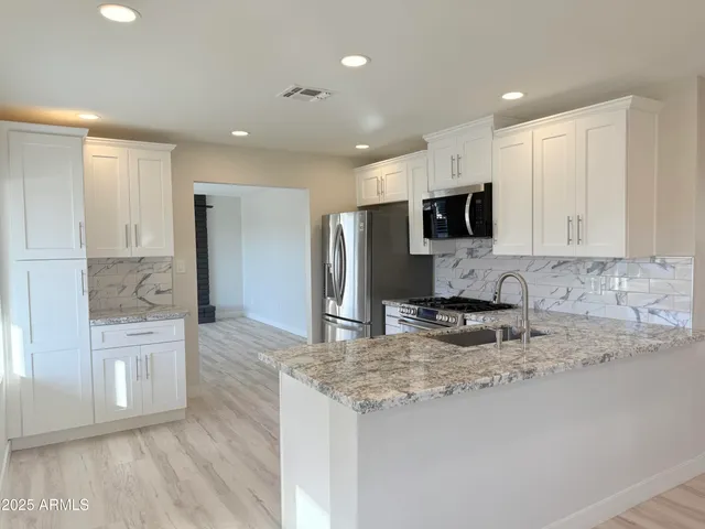 a kitchen with stainless steel appliances granite countertop a stove a sink and a refrigerator with wooden floor