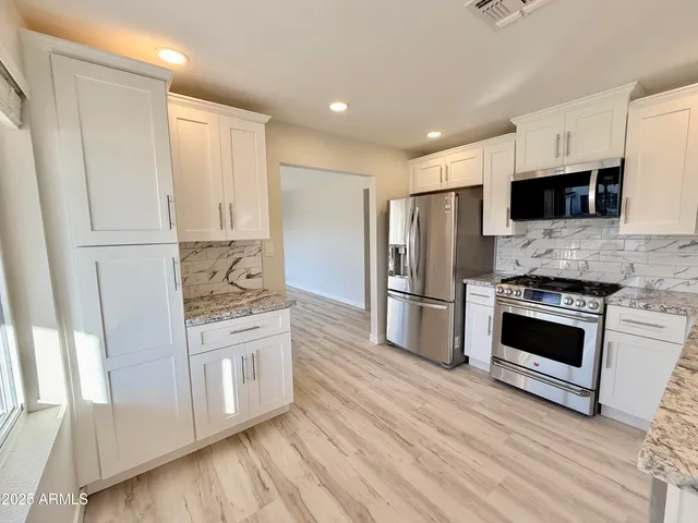 a kitchen with stainless steel appliances a stove a refrigerator a sink and white cabinets