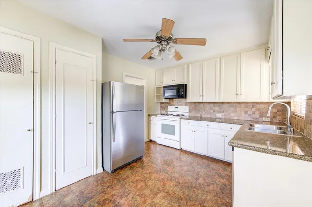 a kitchen with granite countertop a refrigerator a sink a stove and white cabinets