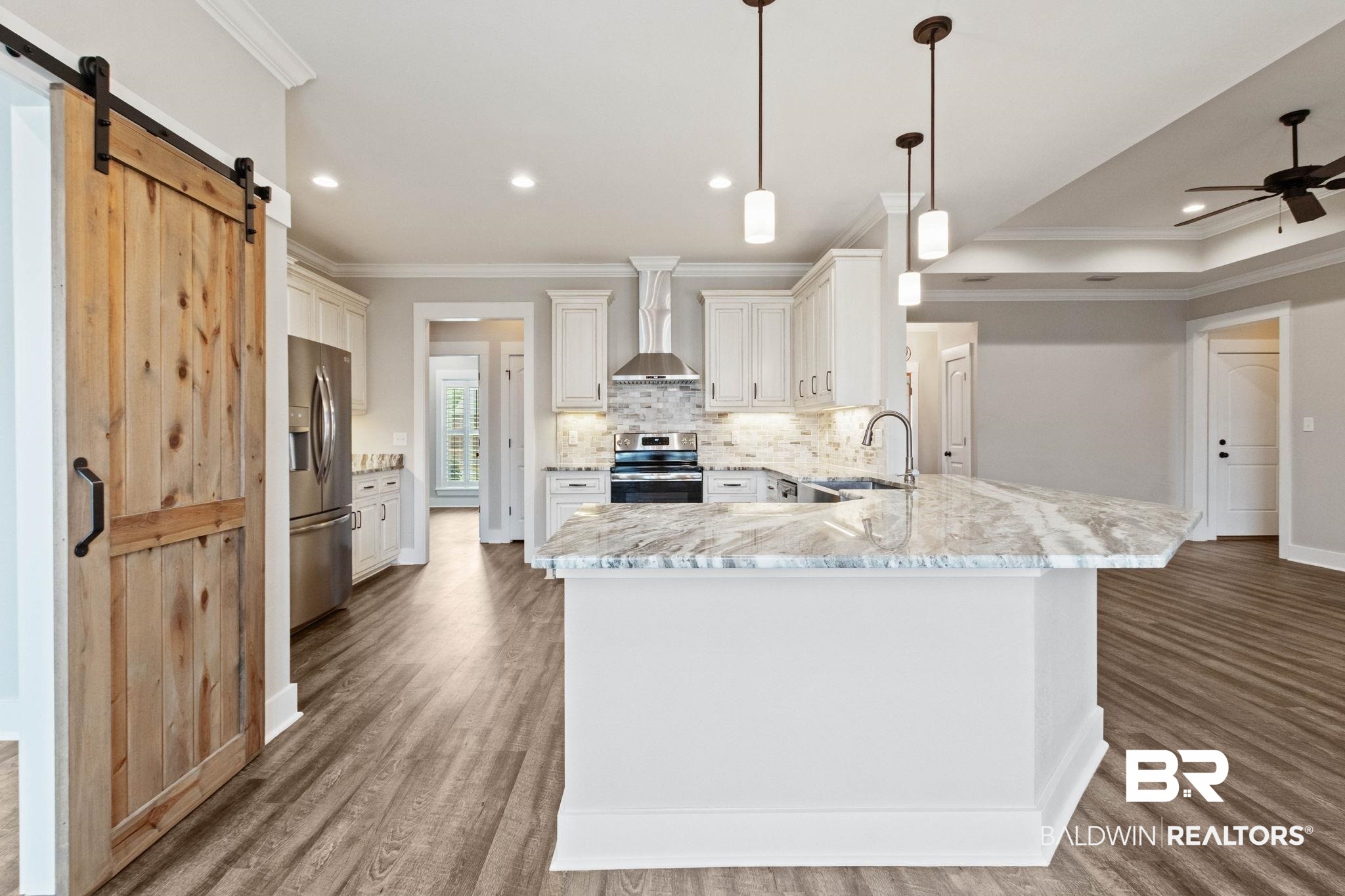 17376 Bankhead Boulevard Fairhope, AL 36532 - Photo 20 of 73 Kitchen featuring ornamental molding, a barn door, a peninsula, stainless steel appliances, and light stone counters