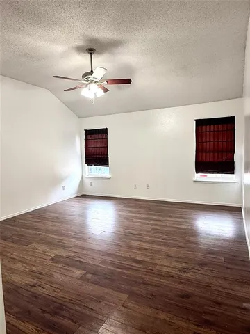 an empty room with wooden floor chandelier fan and windows