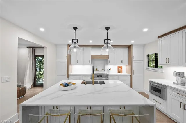 a large kitchen with kitchen island a stove a sink a refrigerator and white cabinets with wooden floor