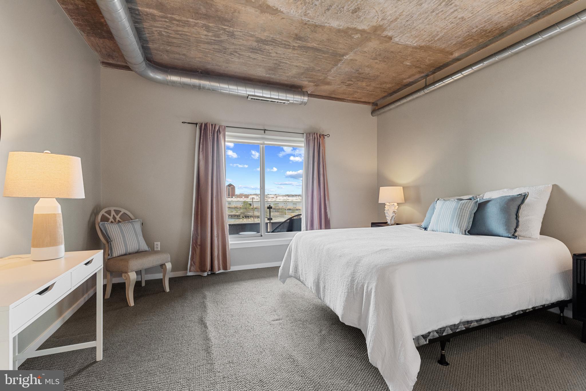 1200 Steuart Street, Unit 416 Baltimore, MD 21230 - Photo 26 of 37 a spacious bedroom with a bed and a lamp on table