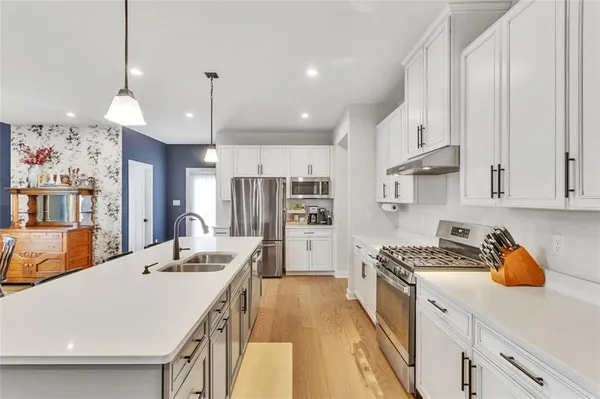 a kitchen with stainless steel appliances a stove a sink a refrigerator white cabinets and couches with wooden floor