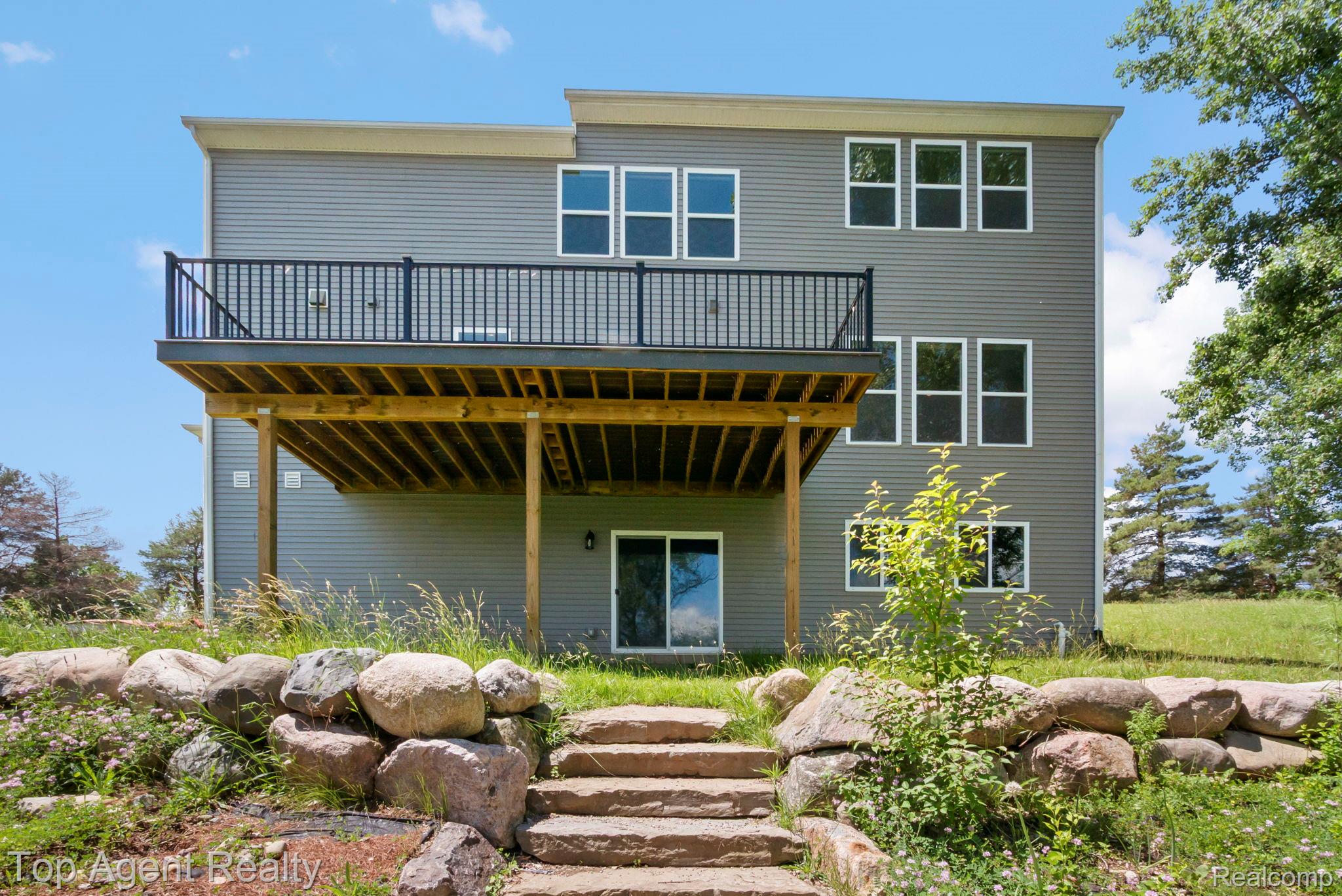 63770 Dequindre Road Washington, MI 48095 - Photo 57 of 61 Rear exterior featuring gray horizontal siding, a wood-finish deck with black railings, and a walk-out basement with a sliding glass door