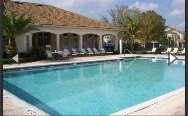 a view of a white house with a large pool and a lawn chairs under an umbrella