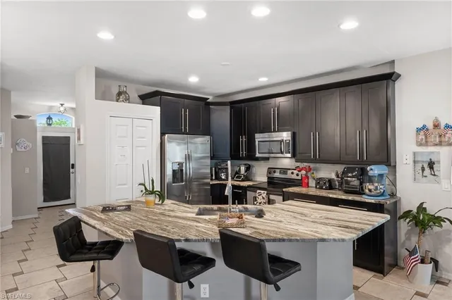 a kitchen with stainless steel appliances kitchen island granite countertop a table chairs sink refrigerator and cabinets