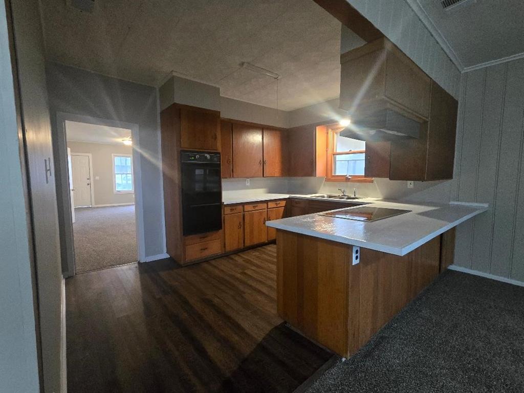 1126 West 6th Avenue Corsicana, TX 75110 - Photo 7 of 12 Kitchen with a peninsula, brown cabinets, light countertops, black appliances, and dark wood-style flooring