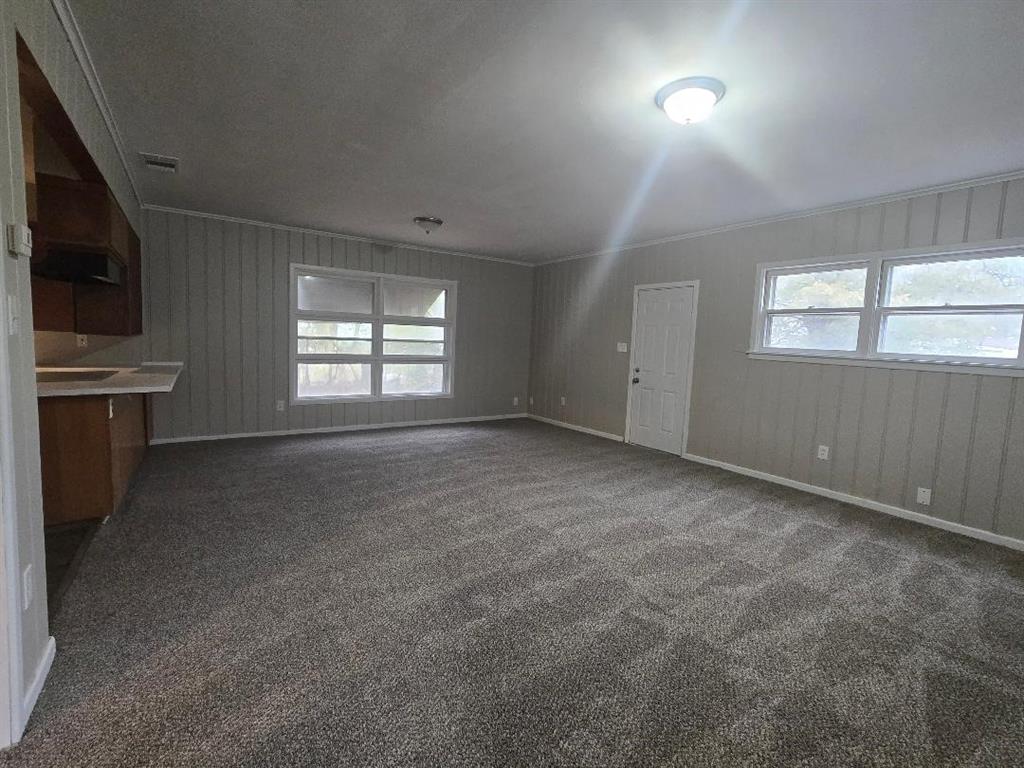 1126 West 6th Avenue Corsicana, TX 75110 - Photo 8 of 12 Unfurnished living room with healthy amount of natural light, dark carpet, and crown molding