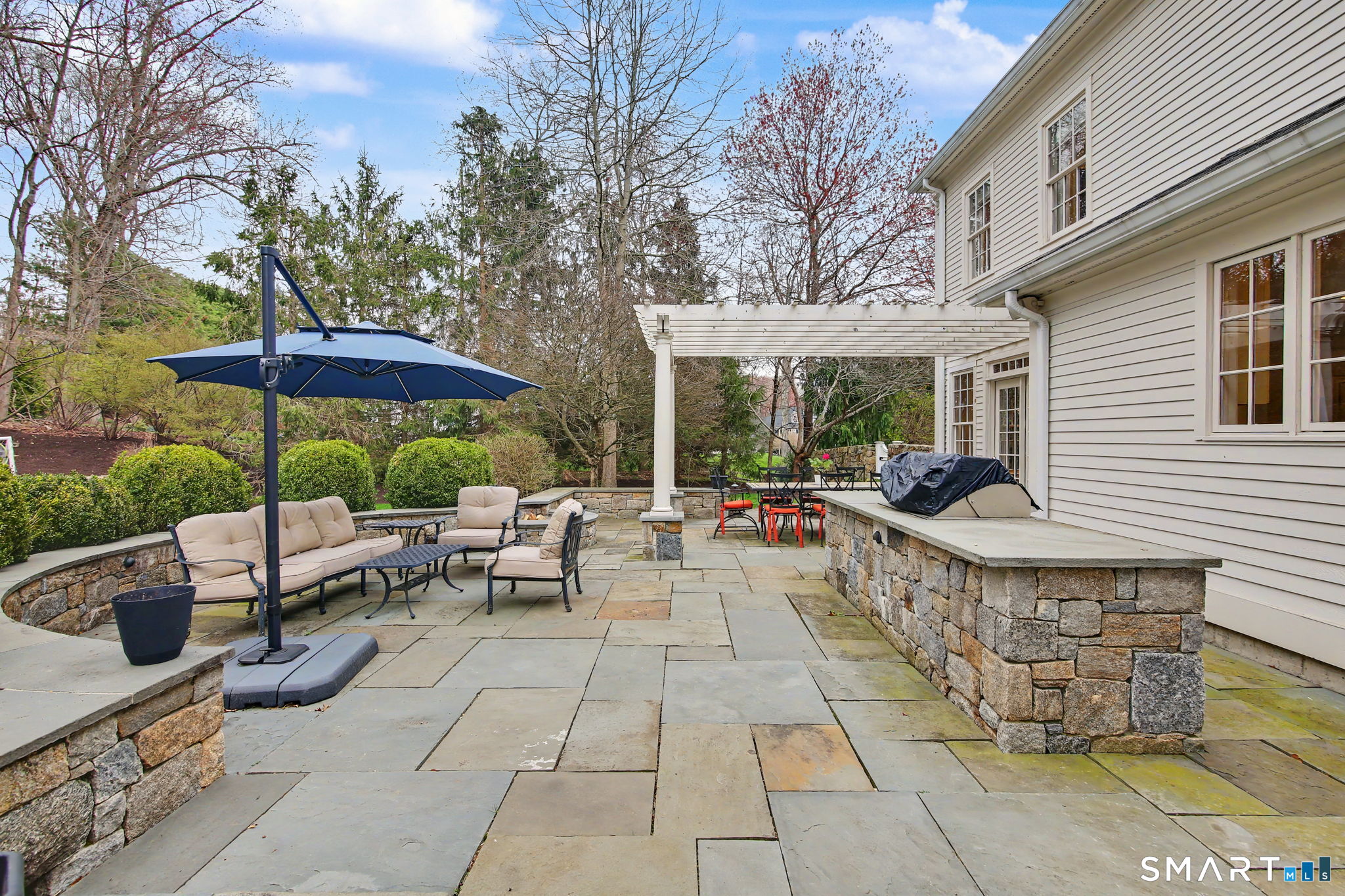 18 Brandon Circle Wilton, CT 06897 - Photo 5 of 40 a view of a patio with couches table and chairs under an umbrella with a barbeque