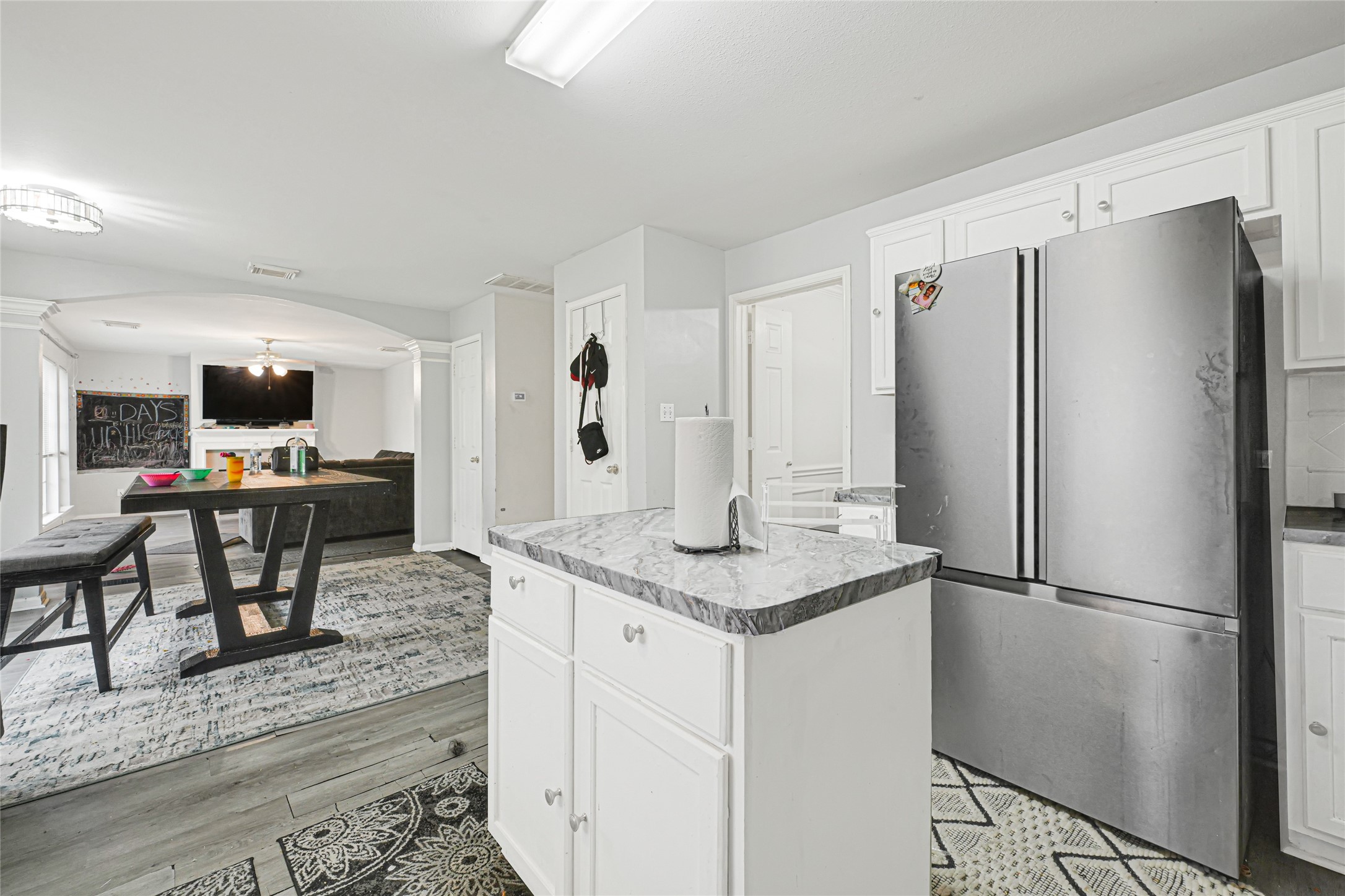 6419 Slate Stone Street Houston, TX 77084 - Photo 12 of 49 This photo showcases a modern, open-concept kitchen and living area featuring white cabinetry, a marble countertop island, and stainless steel appliances. The space is bright with ample natural light and includes a dining area and a cozy living room with a fireplace and mounted TV.