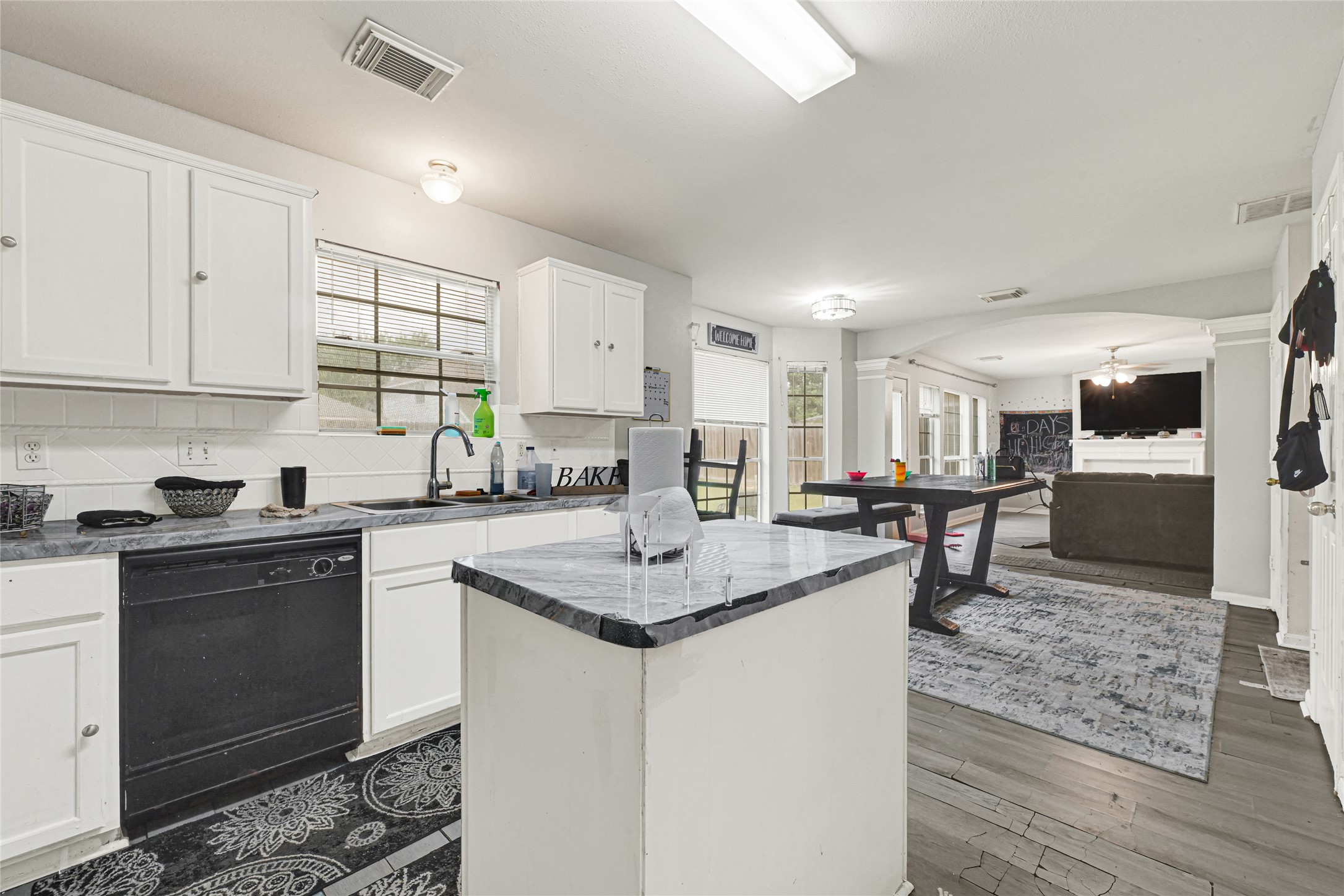 6419 Slate Stone Street Houston, TX 77084 - Photo 13 of 49 This open-concept kitchen and living area features white cabinetry, a central island, and dark countertops. The space flows into a dining area with large windows offering natural light, and a cozy living room with a wall-mounted TV.