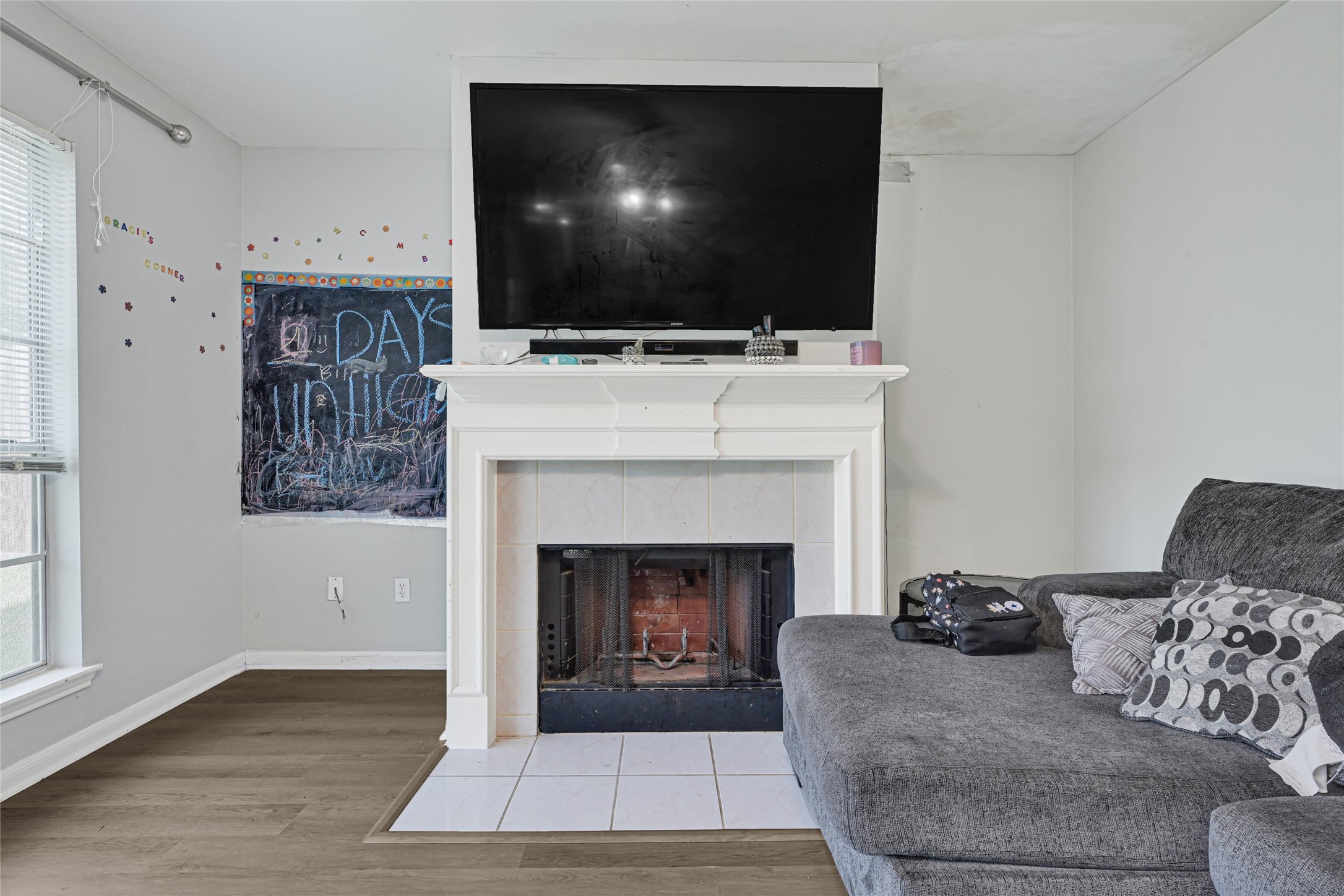 6419 Slate Stone Street Houston, TX 77084 - Photo 14 of 49 Cozy living space featuring a fireplace with a mounted TV above, adjacent to a large window allowing natural light. The room includes a comfortable sectional sofa and a chalkboard wall for creative expression.